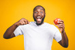 © denis_vermenko - Man with tooth brush. Image of young shirtless African man holding a toothbrush with toothpaste and apple, smiling while standing against yellow background.