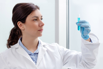 young female scientist looking at a test-tube containing blue liquid