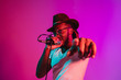 © master1305 - Young african-american jazz musician with microphone singing a song on purple studio background in trendy neon light. Concept of music, hobby, inspirness. Colorful portrait of joyful attractive artist