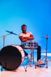 © master1305 - Young african-american jazz musician or drummer playing drums on blue studio background in trendy neon lights. Concept of music, hobby, inspirness. Colorful portrait of joyful attractive artist.