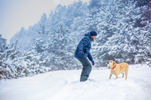 A Man And Dog Are Best Friends. The Man With The Dog Playing In A Snowy Pine Forest In Winter
