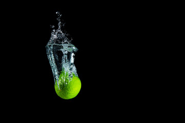 Wall Mural - Fresh and delicious lime isolated against dark, black background. Lime dropping in water and creating a splash. The concept of healthy eating, consuming fruit.