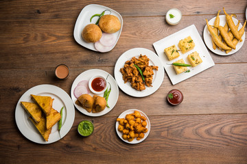 Canvas Print - Indian Tea time snacks  in group includes Veg Samosa, Kachori/kachaudi, aloo bonda, khaman dhokla, bread, onion,chilli and moong pakora/pakoda/bhaji/bhajji/Bhajiya/bajji with sauces, selective focus