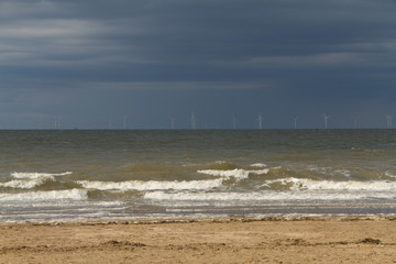 Large offshore wind farm on the horizon as seen from a sandy beach