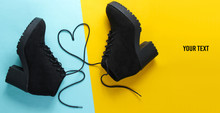Black suede boots with heart-shaped laces on blue yellow background. copy space. Top view
