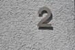 © Hermann - Hausnummer 2 aus Metall an einer verputzten, grau gestrichenen Hauswand