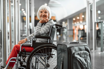 Happy mature lady on disabled carriage waiting for trip at hall