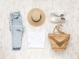 Wall Mural - White t-shirt, light blue ripped jeans, white sneakers, wicker bag, straw boater hat on white wooden background. Overhead view of woman's casual day outfit. Trendy spring or summer look. Flat lay.