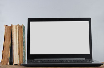 Wall Mural - Modern laptop and stack old books  on wooden shelf against the white wall background. Old and new sources of information.