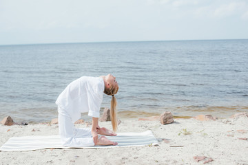 Wall Mural - pretty woman with closed eyes practicing yoga on yoga mat near sea