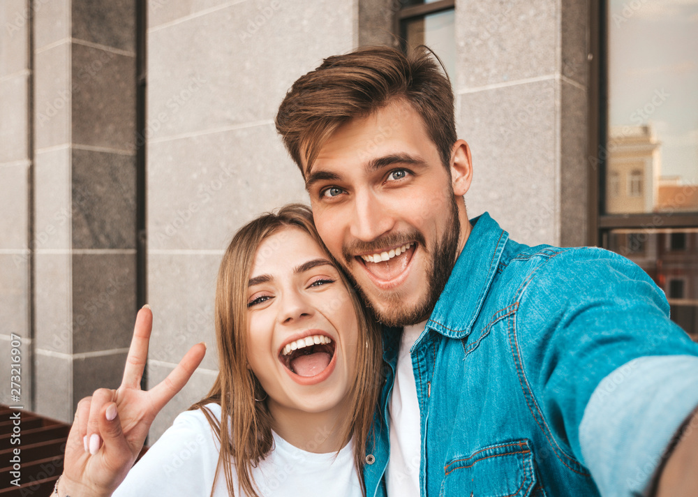 Smiling beautiful girl and her handsome boyfriend in casual summer clothes. Happy family taking selfie self portrait of themselves on smartphone camera. Having fun on the street background - obrazy, fototapety, plakaty 
