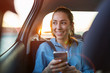 © pikselstock - Young woman with smartphone on the back seat of a car