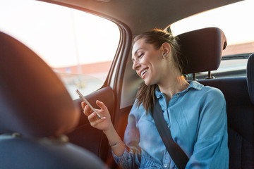 Wall Mural - young woman with smartphone on the back seat of a car