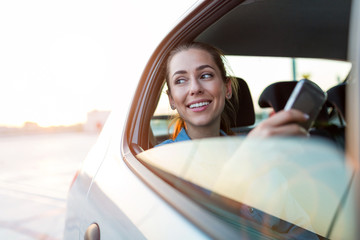 Wall Mural - young woman with smartphone on the back seat of a car