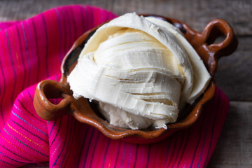 Fresh Oaxaca cheese in clay pot on wood background