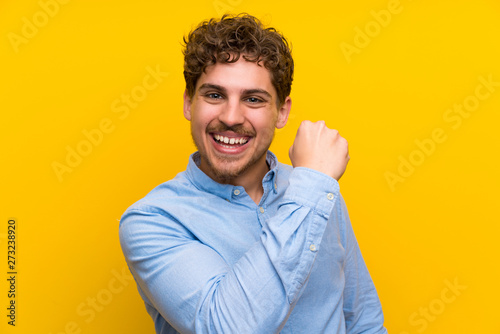 Photographie Blonde man over isolated yellow wall celebrating a victory