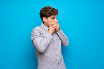 Wall Mural - Blonde man over blue wall covering mouth and looking to the side