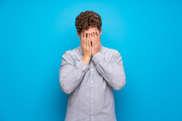 Wall Mural - Blonde man over blue wall with tired and sick expression