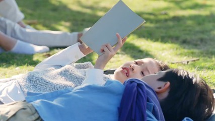 Wall Mural - beautiful little asian girl and boy sister and brother lying on grass reading a book together in park