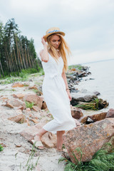 Wall Mural - beautiful blonde woman standing and touching straw hat near sea