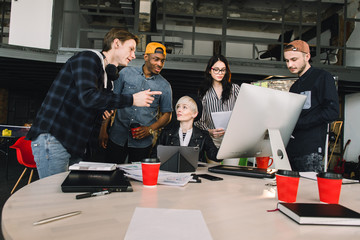 Wall Mural - Young six people working in positive environment in loft office, woman sitting at the table and using computer