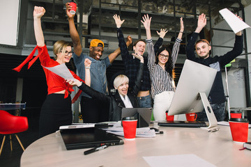 Wall Mural - Great news. Happy smiling businesspeople in casual clothes triumphing with arms up while looking at laptop and computer in modern office