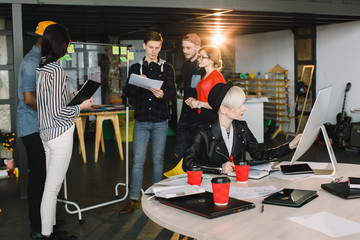 Wall Mural - Business people meeting at office and share ideas on the glass wall. Brainstorming concept. Young woman in black hat and jacket sitting at the table and working with computer