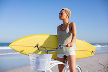 Woman With Surfboard Sitting On Bicycle At Beach In The Sunshine