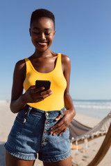 Woman using mobile phone with her thumbs in belt loops on the beach