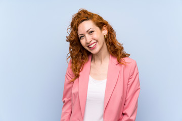 Redhead woman in suit over isolated blue wall smiling