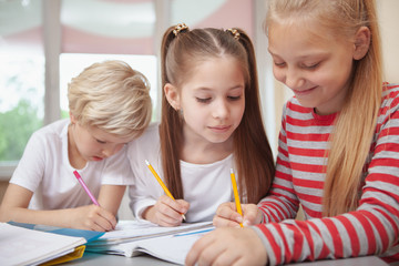 Three lovely shoolgirls chatting during elementary school drawing lesson. Beautiful little girl looking at her friend sketching. Education, friendship, interaction concept