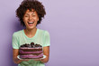 © wayhome.studio  - Happy birthday girl laughs joyfully, holds big tasty fruit cake, likes eating sweet food, improves mood with raising sugar in blood, has positive face look, stands over purple background, blank space