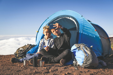 two boys taking selfie sitting in a camping tent couple of young tourists enjoying high mountain vac