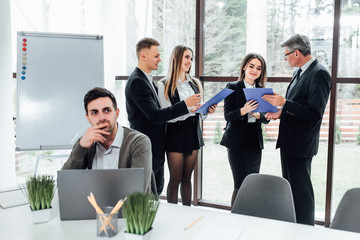 Wall Mural - Group of successful  businesspeople using a folder  together in front of office building windows overlooking the city..