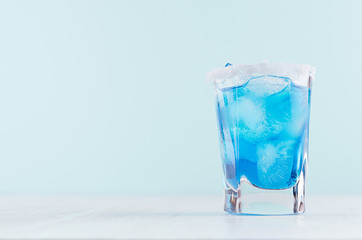 Exquisite blue cocktail for celebration in beach style with blue curacao, ice cube, sugar rim in mint color bar interior on white wood table.