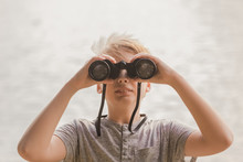Closeup Front View Of Cute Caucasian Kid Holding Old Vintage Binoculars In Hands And Looking Forward At Something Far Away. Horizontal Color Photography.