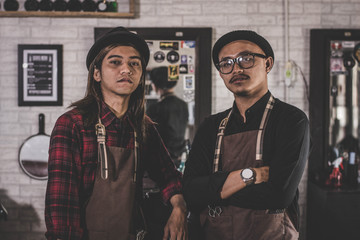 portrait of two stylist barber hairdresser with apron standing at barbershop.