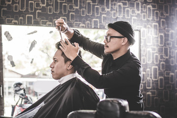 Wall Mural - Portrait of barber making hair cut of his attractive man in barbershop