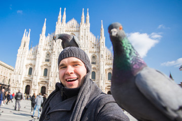 Winter travel, vacations and birds concept - Young funny man taking selfie with pigeons near Milan Cathedral Duomo di Milano, Italy.