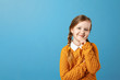 © Olga - Portrait of a little girl schoolgirl in a yellow sweater on a blue background. Pensive child holding hand on chin and looking at camera. Copy space