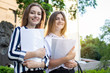 © Богдан Маліцький - two pretty students are standing near the university, holding papers in their hands and smiling against the background of the college, they go to school