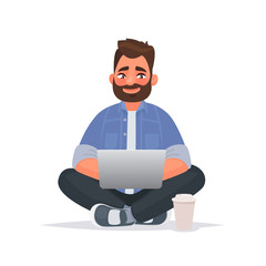 Wall Mural - Bearded man sits on the floor and works at a laptop. Remote work via the Internet. Freelancer