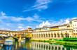 Ponte Vecchio bridge with colourful buildings houses over Arno River blue reflecting water and embankment promenade archways, historical centre of Florence city, blue sky white clouds, Tuscany, Italy
