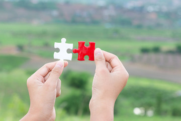 hands holding piece of red and white jigsaw puzzle. teamwork concept