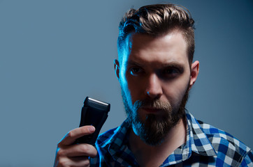 Handsome bearded man holding electric shaver in his arm, closeup portrait studio shot 