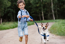 Happy Boy With Dog On Leash Running At Country Road