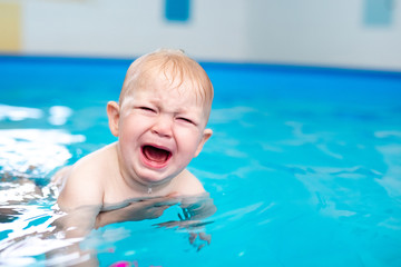 Cute sad baby boy learning to swim in special pool for little children