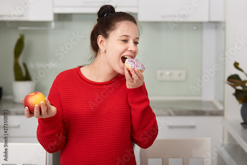 Pregnant woman in kitchen holding apple in hand and eating cake ... Pregnant woman in kitchen holding apple in hand and eating cake ...
