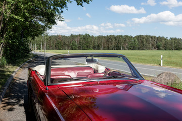 Red old Ford Mustang cabriolet is parked at the roadside