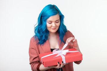 Wall Mural - People, holidays and fashion concept - Happy young woman with blue hair holding a gift box on white background